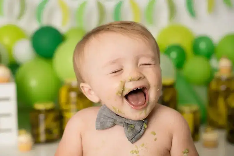 Baby laughing at a pickle-themed birthday celebration with green decorations.