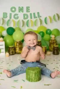 Baby celebrating first birthday with pickle-themed decorations and cake.