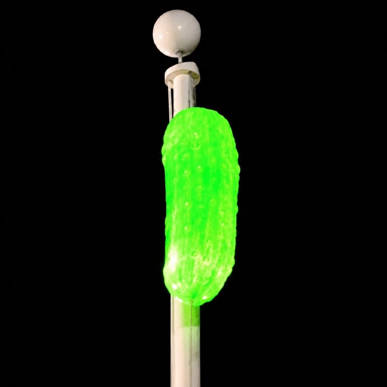 Glowing green pickle-shaped light on a pole for New Year's Eve celebration.