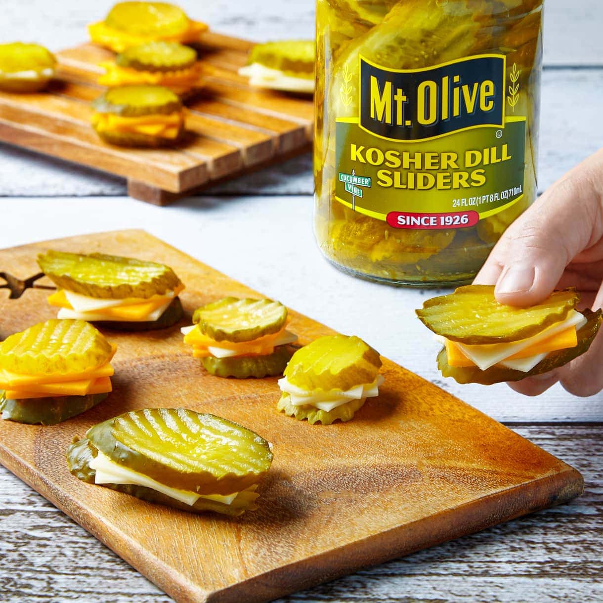 wood cutting board with pickle and cheese snackers.Kosher Dill Slider Pickles with slices of cheese on them like mini sandwiches.