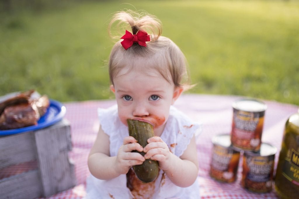 Baby eating large whole pickle at picnic