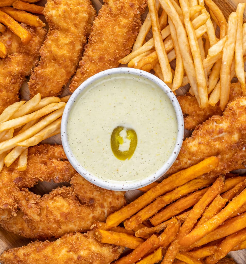 Dish of ranch dressing topped with jalapeno surrounded by chicken tenders and french fries