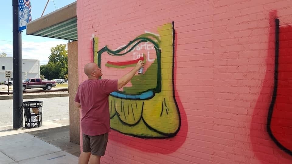 Artist painting a colorful mural on a pink brick wall in downtown area.
