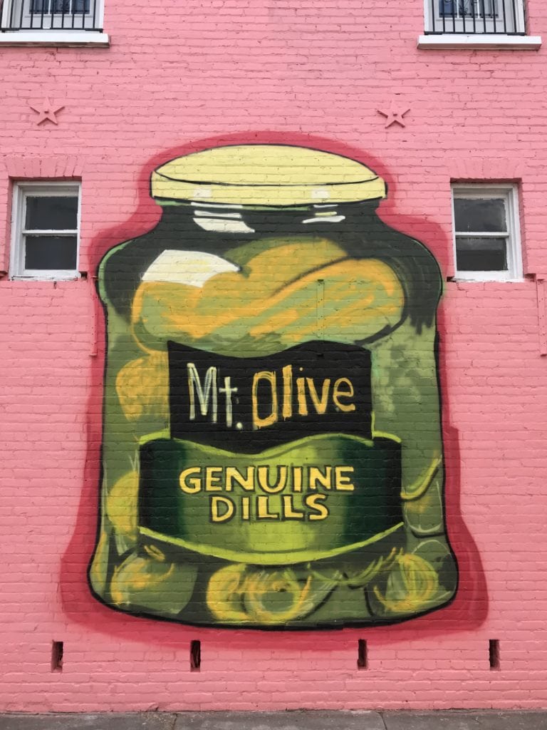 Colorful mural of Mt Olive Pickles jar on pink building wall.