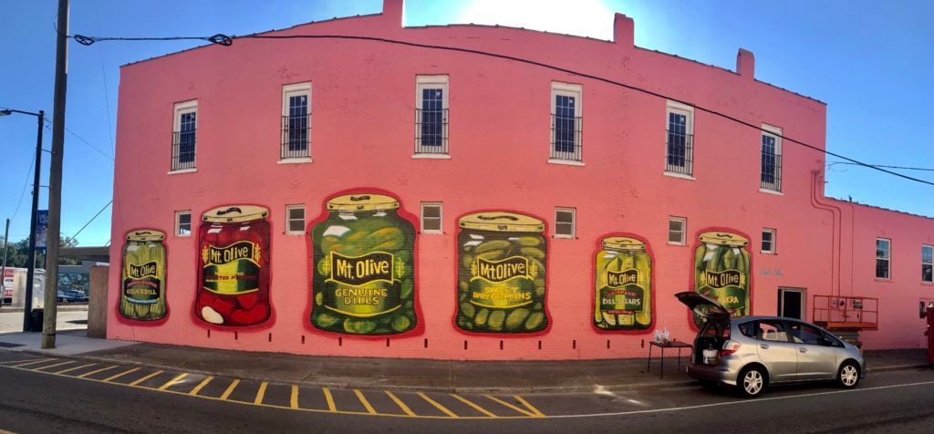 Colorful mural of Mt Olive Pickles jars on pink building wall in downtown area.