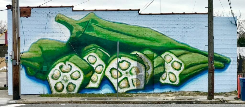 Colorful mural of green okra and pickles on a brick wall.