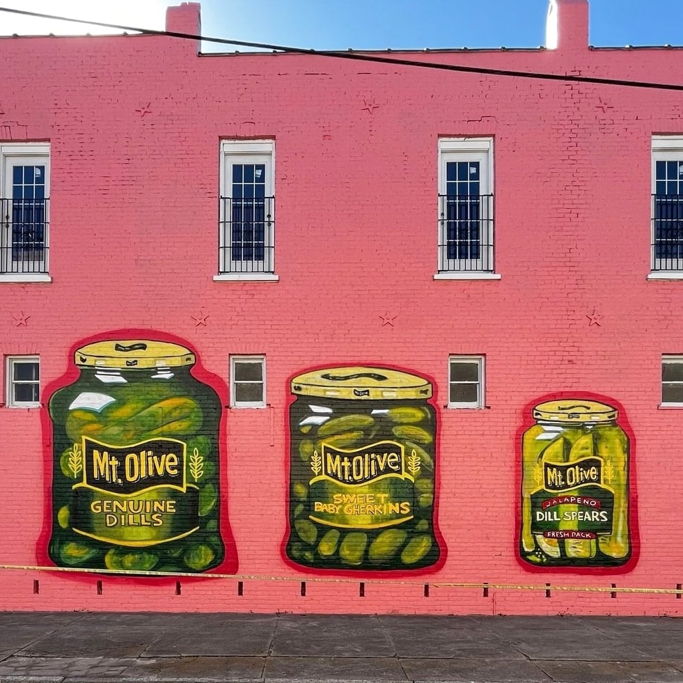 Colorful mural of Mt Olive pickle jars on a pink building wall.