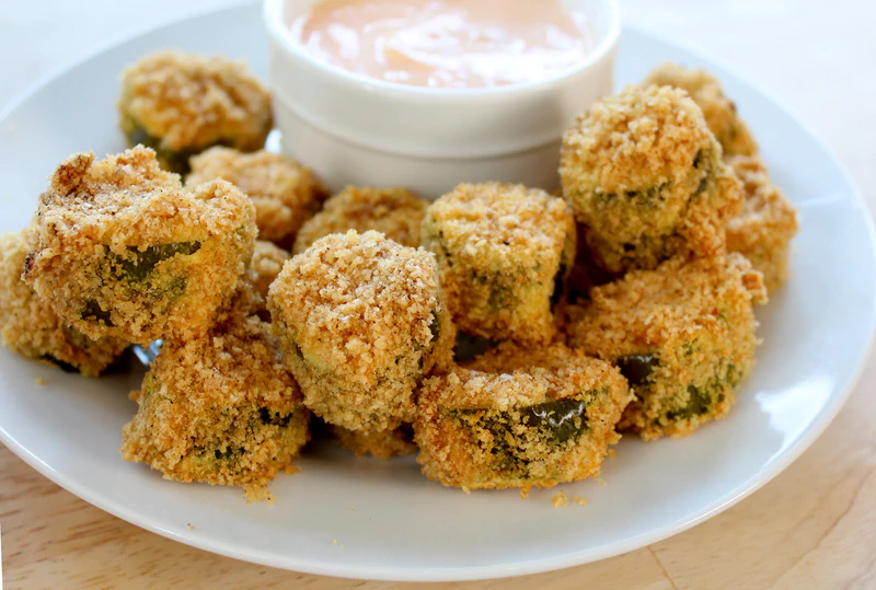 fried pickles on a white plate with dish of dipping sauce