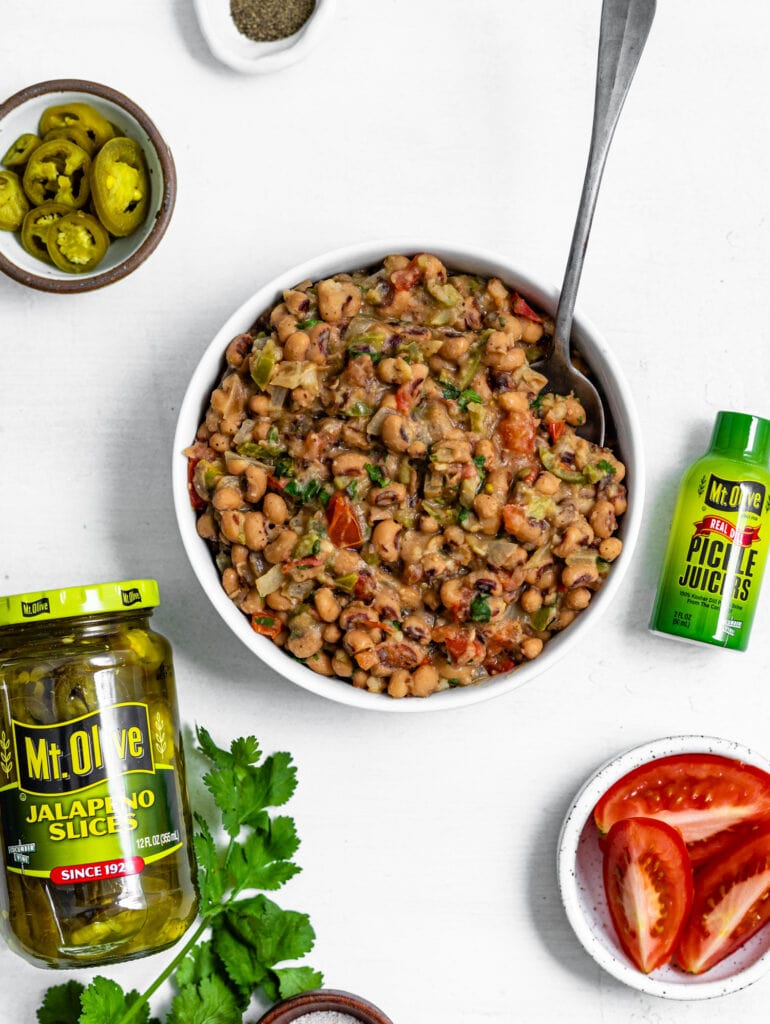 white bowl with black eyed peas mixture. next to bowl is jar of jalapenos and a Pickle Juicer 2 oz bottle