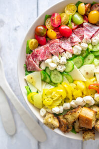 close up of salad with tomatoes, salami, cucumbers, mozzarella cheese balls, banana peppers and croutons