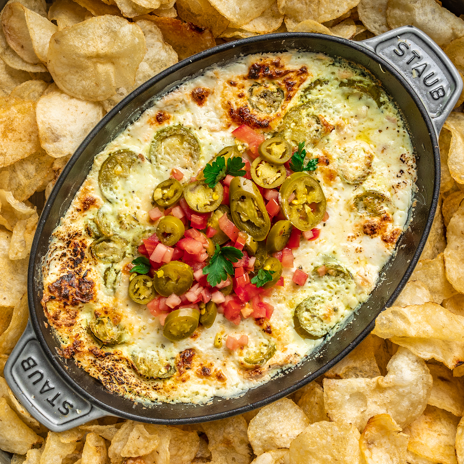 dutch oven with melted cheese topped with jalapenos and tomatoes surrounded by potato chips