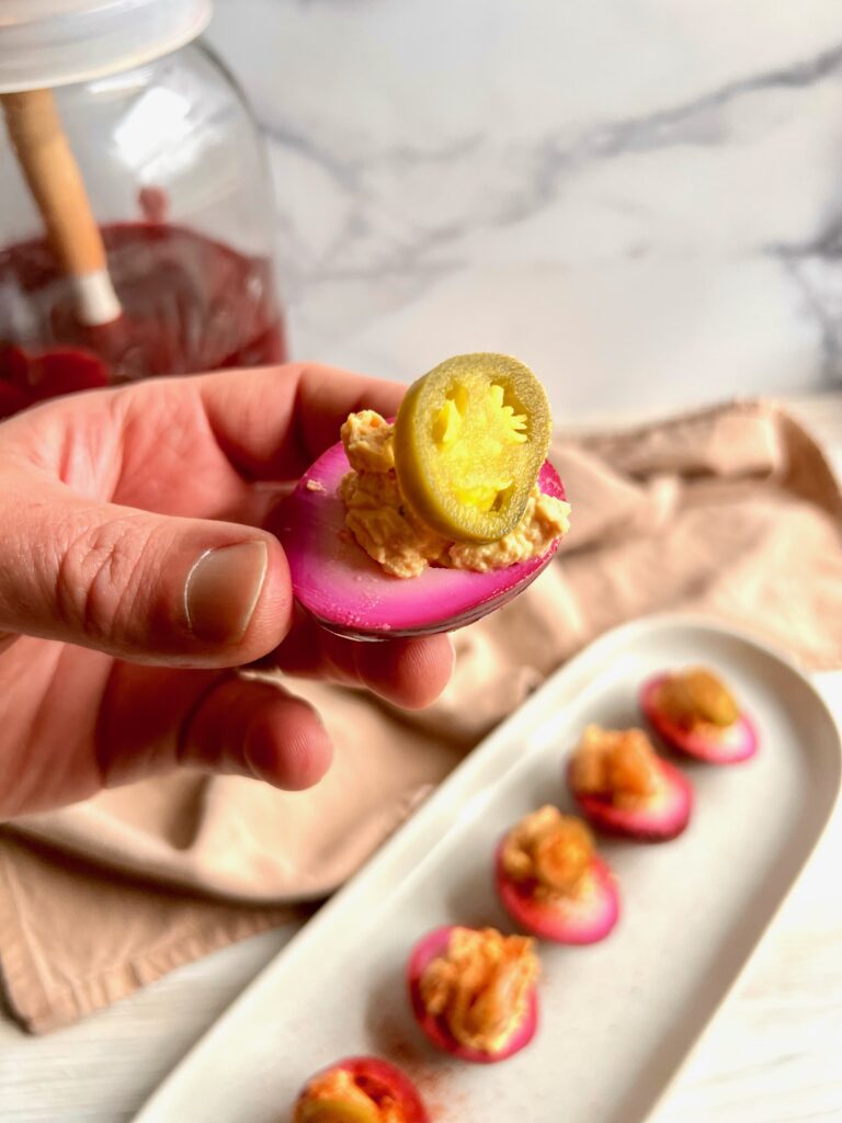 a purple deviled egg with a jalapeno slice on top. held by a man's hand.
