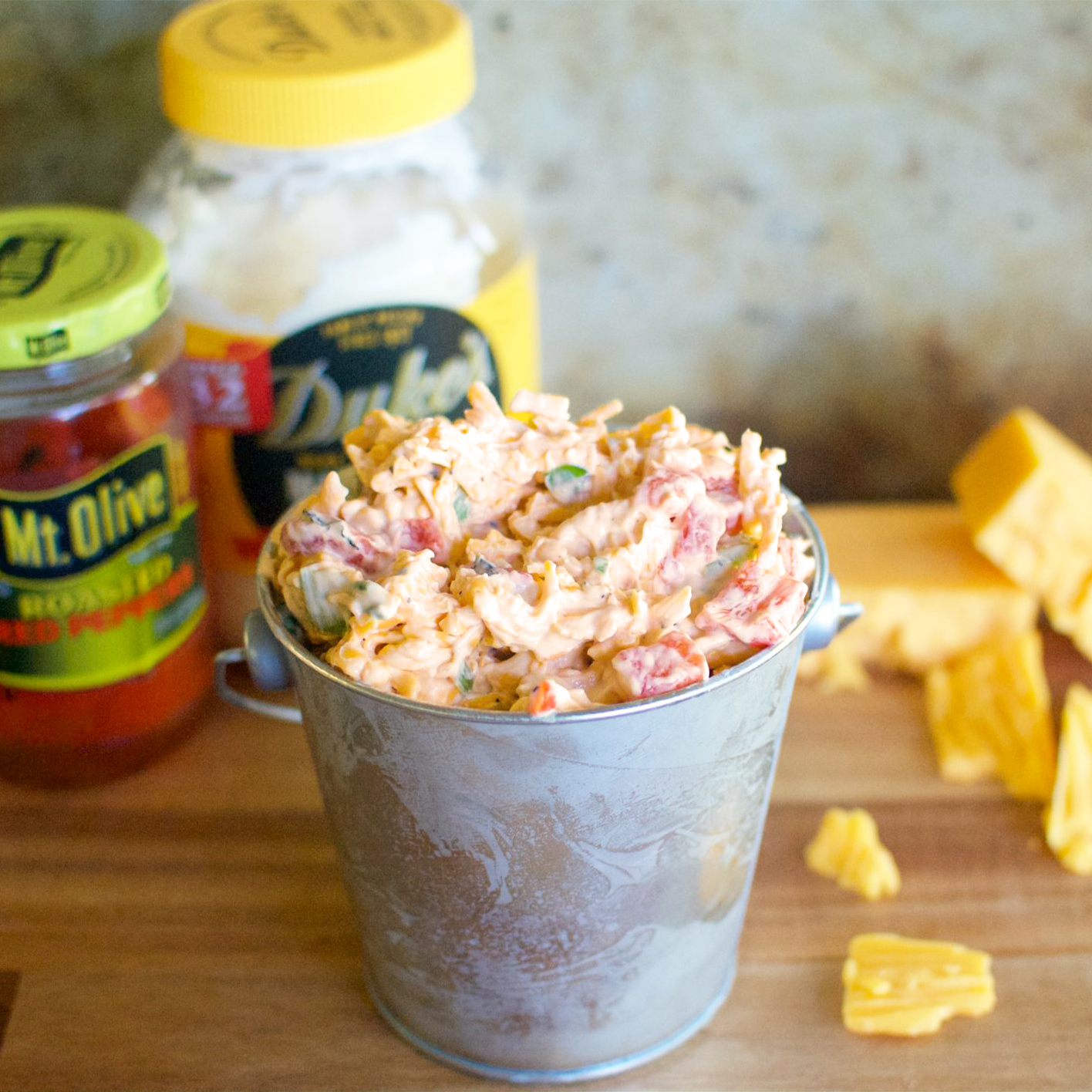 small metal bucket loaded with pimento cheese mixture. background shows jar of Mt. Olive Roasted Red peppers and jar of Duke's Mayo