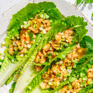 white plate with large romaine lettuce leaves filled with shrimp, jalapenos and corn (shrimp lettuce wraps)