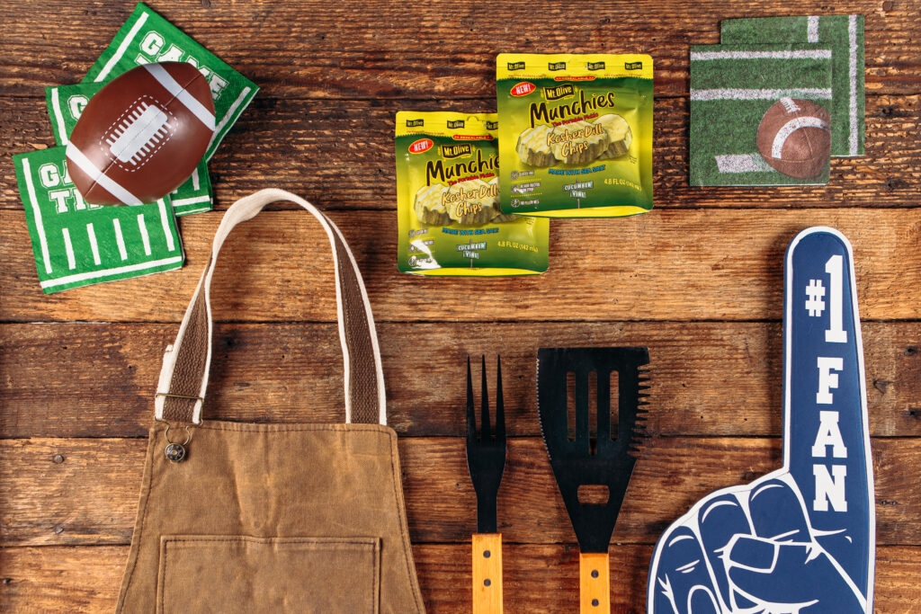 wood background with football decor, grilling tools, apron and Munchies Pickle Pouches