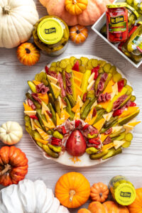platter of charcuterie items like cured meats, cheese, pickles, okra, pear arranged to look like a turkey and surrounded by pumpkins and jars of Mt. Olive products