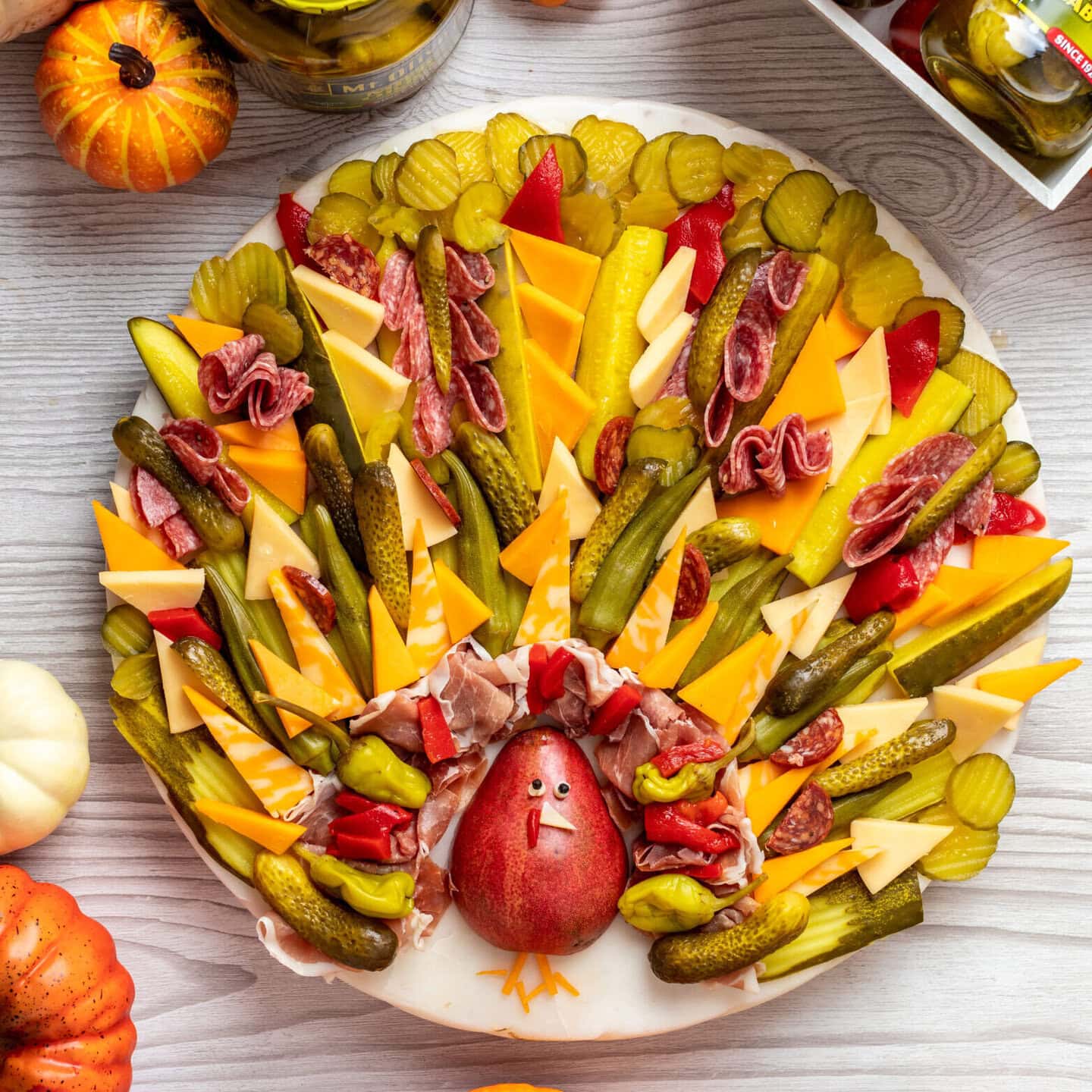 platter of charcuterie items like cured meats, cheese, pickles, okra, pear arranged to look like a turkey and surrounded by pumpkins and jars of Mt. Olive products