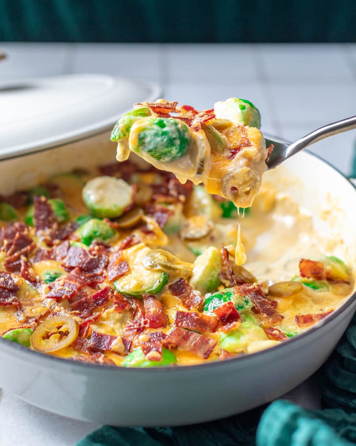 white dish with spoon holding contents of dish. Jalapeno Brussels Sprouts Gratin shows cheesy brussels sprouts with jalapenos