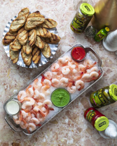 shrimp cocktail with three sauces (white, green and red sauce dishes) and a plate of grilled bread