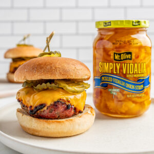 cheeseburger with pickle chips on a white plate next to a jar of Simply Vidalia Onions