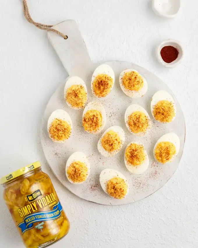 Deviled eggs topped with paprika and pickles on a white platter.