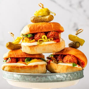 three meatball sliders on a metal tray. meatballs, cheese, and peppers on them.