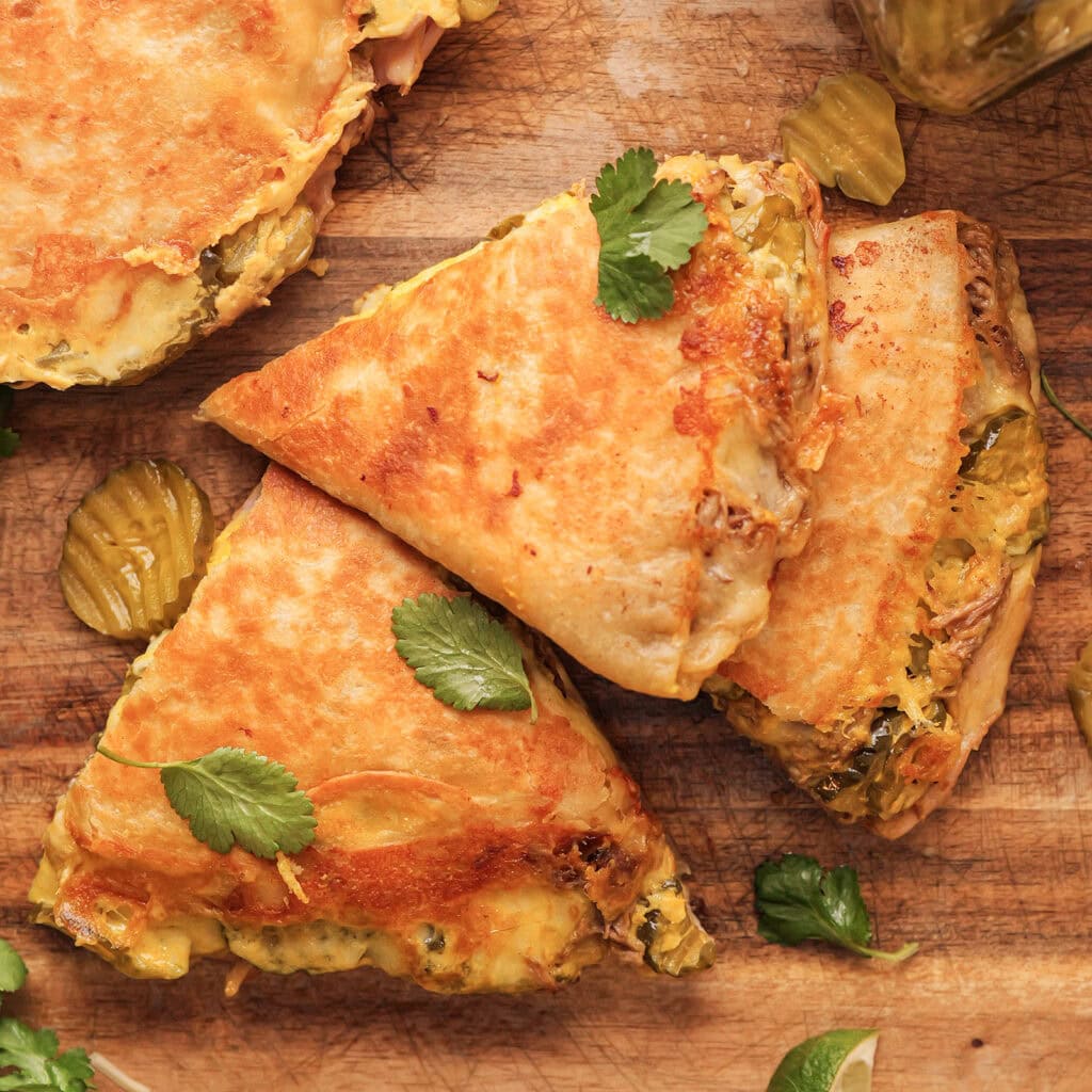 A close up of a Cubano Quesadilla on a wood board. Pickles are showing.