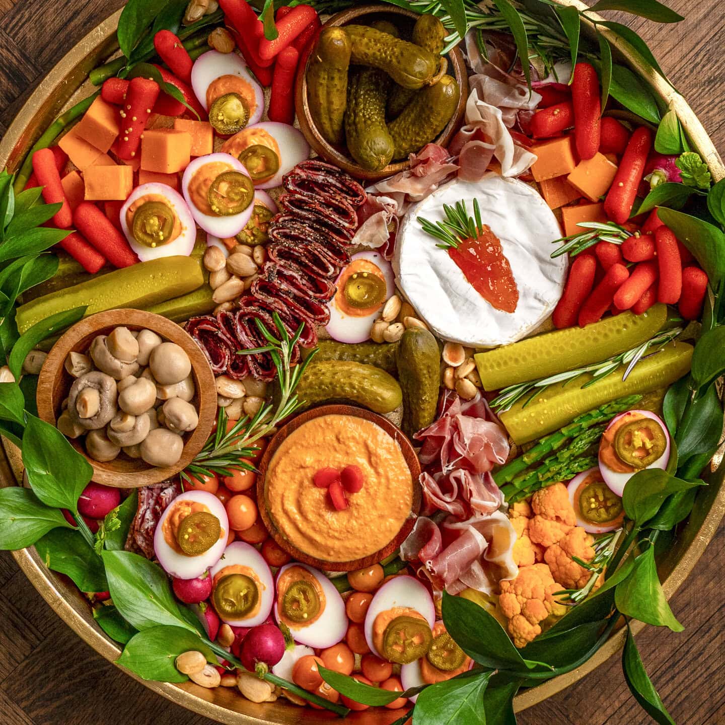 A charcuterie board with carrot shape in brie, orange carrot hummus, assortment of pickles and pickled peppers, deviled eggs, etc.