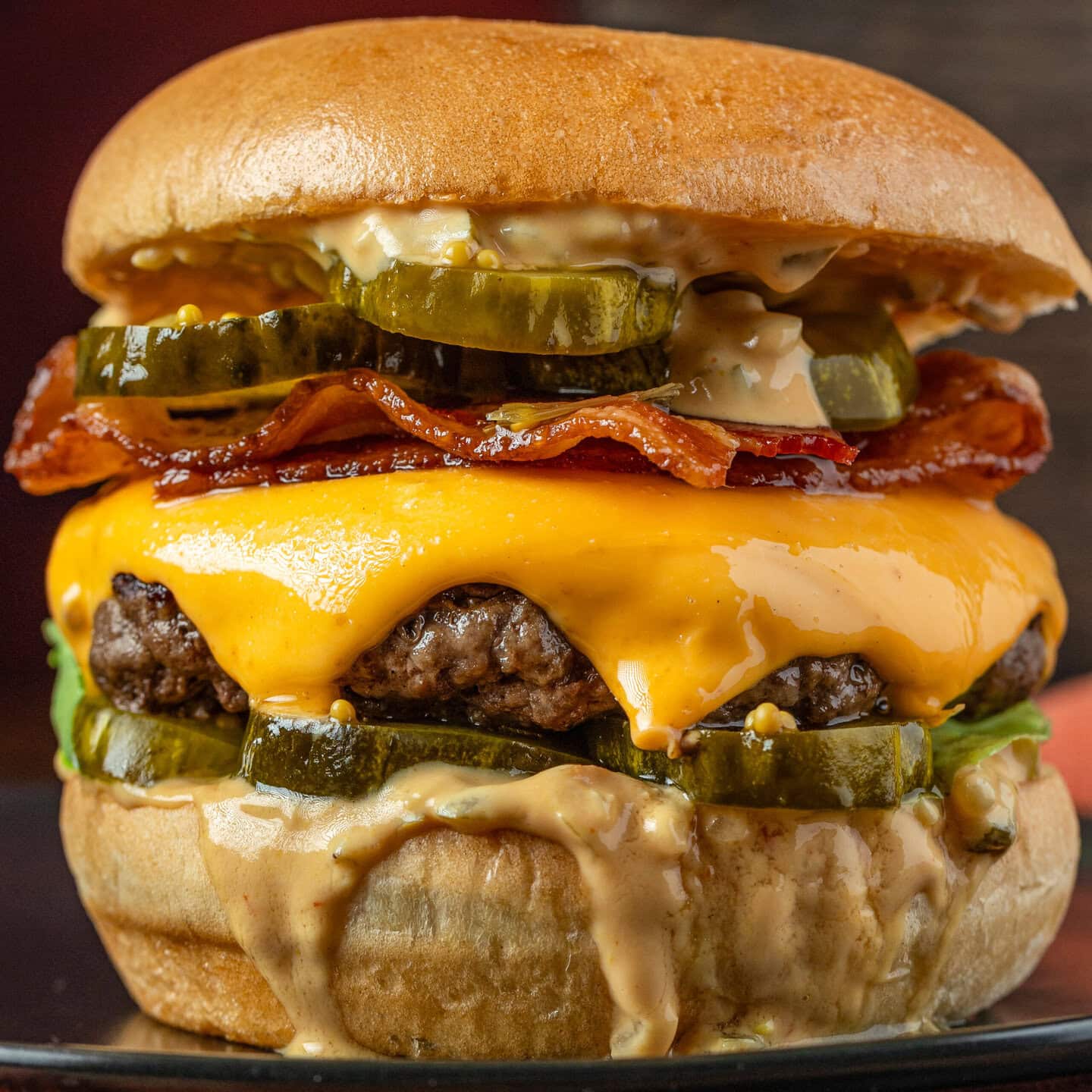 A close up of a cheeseburger with lots of pickles and bacon, dripping with Majestic Burger Sauce.