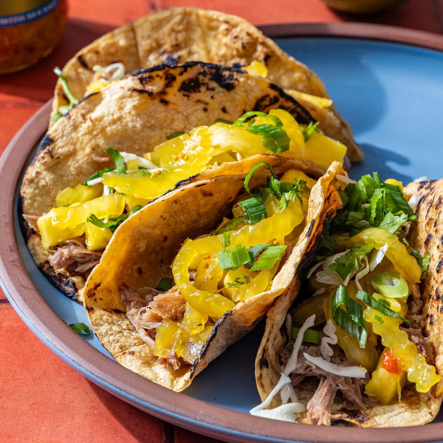 A plate with several tacos that have pulled pork and pickled sweet onions on top.
