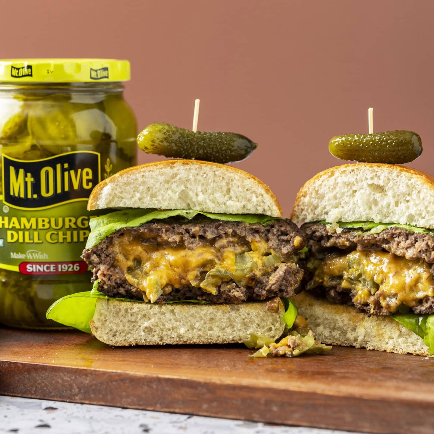 A stuffed burger cut in half, with cheese and pickles dripping out. It&rsquo;s topped with a petite pickle.