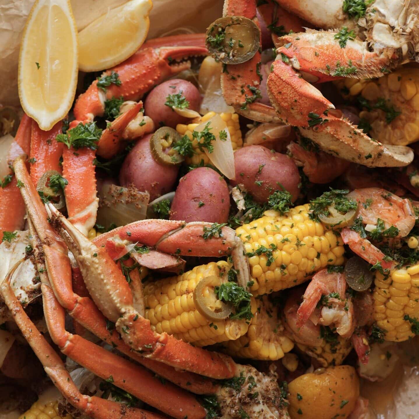 A seafood boil containing crab legs, Mt. Olive jalapenos, corn, potatoes, shrimp,and lemon wedges.