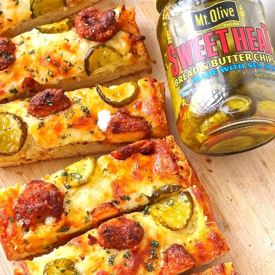 Cheesy Nashville Hot Chicken Garlic Bread on a wooden board next to jar of sweet heat pickles.