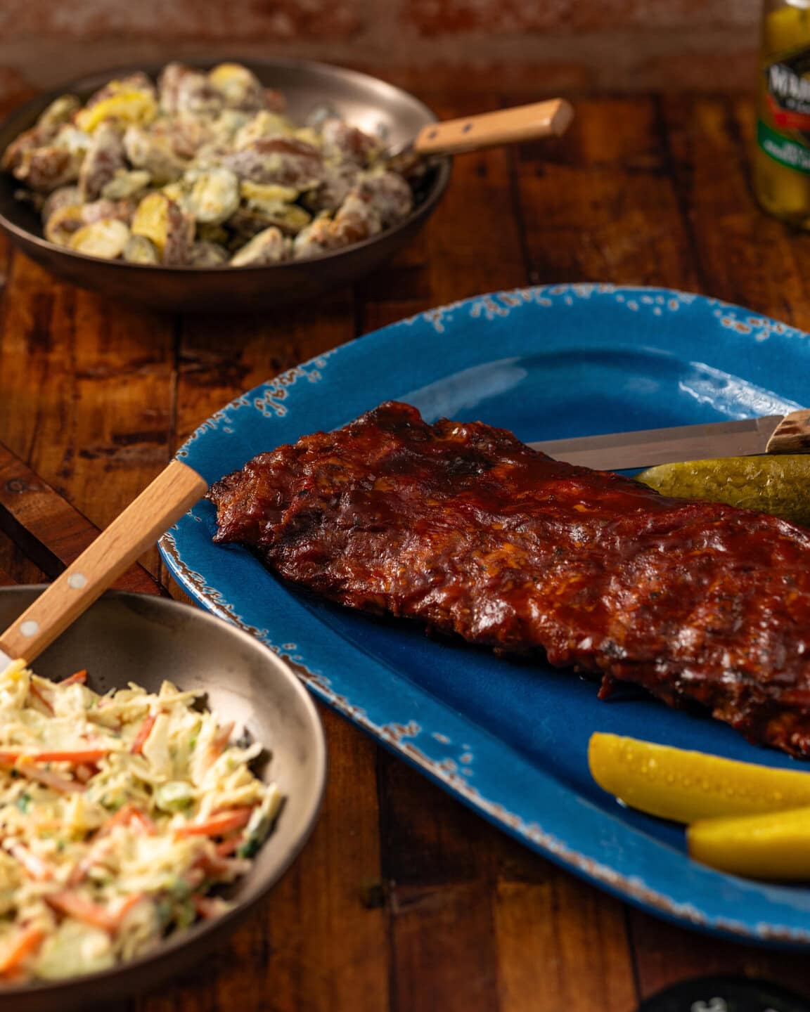 A blue plate of baby back ribs with coleslaw and potatoes.