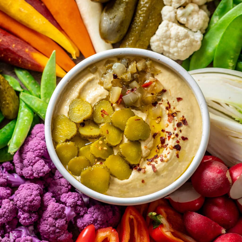 A bowl of pickle hummus surrounded by assorted raw vegetables.