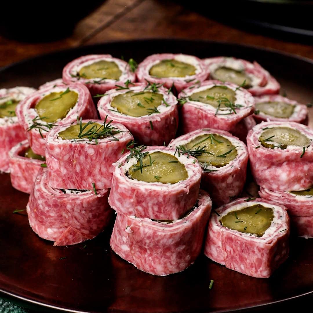 Salami and Mascarpone Pickle Pinwheels topped with fresh dill sitting on a plate.