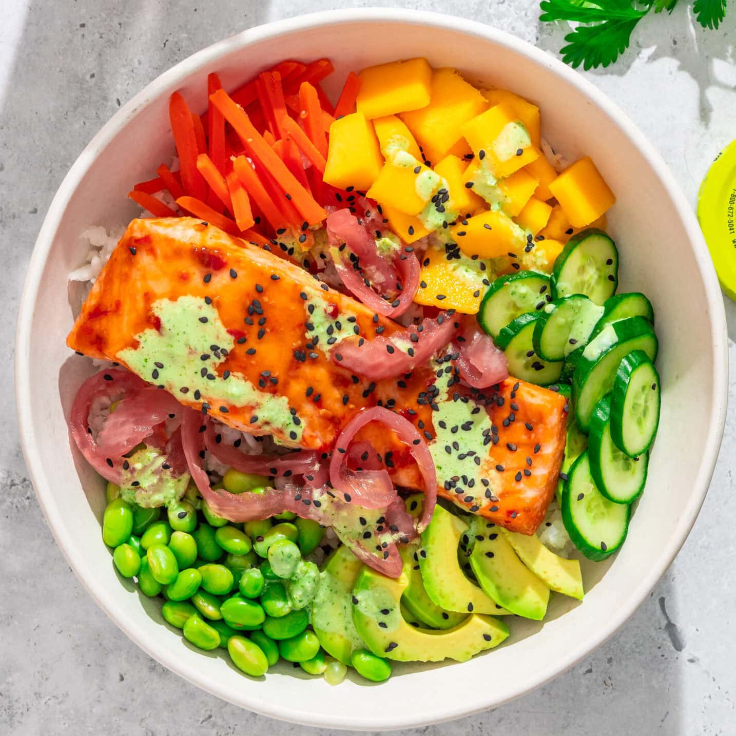Spicy salmon bowl with avocado, cucumber, mango, carrots, edamame, and pickled red onions.