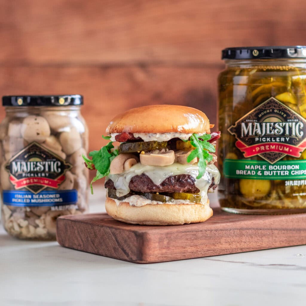 Mushroom Swiss Burger on a wood cutting board with two Majestic Picklery jars.