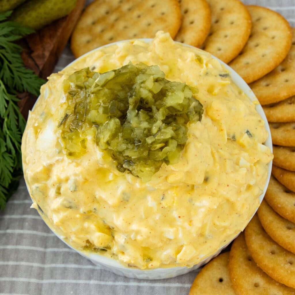 A bowl of Deviled Egg Dip topped with relish and served with crackers.