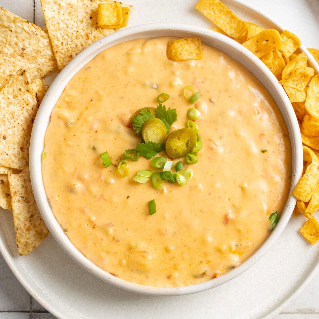 A bowl of jalapeno queso dip topped with green onions and pickled peppers.