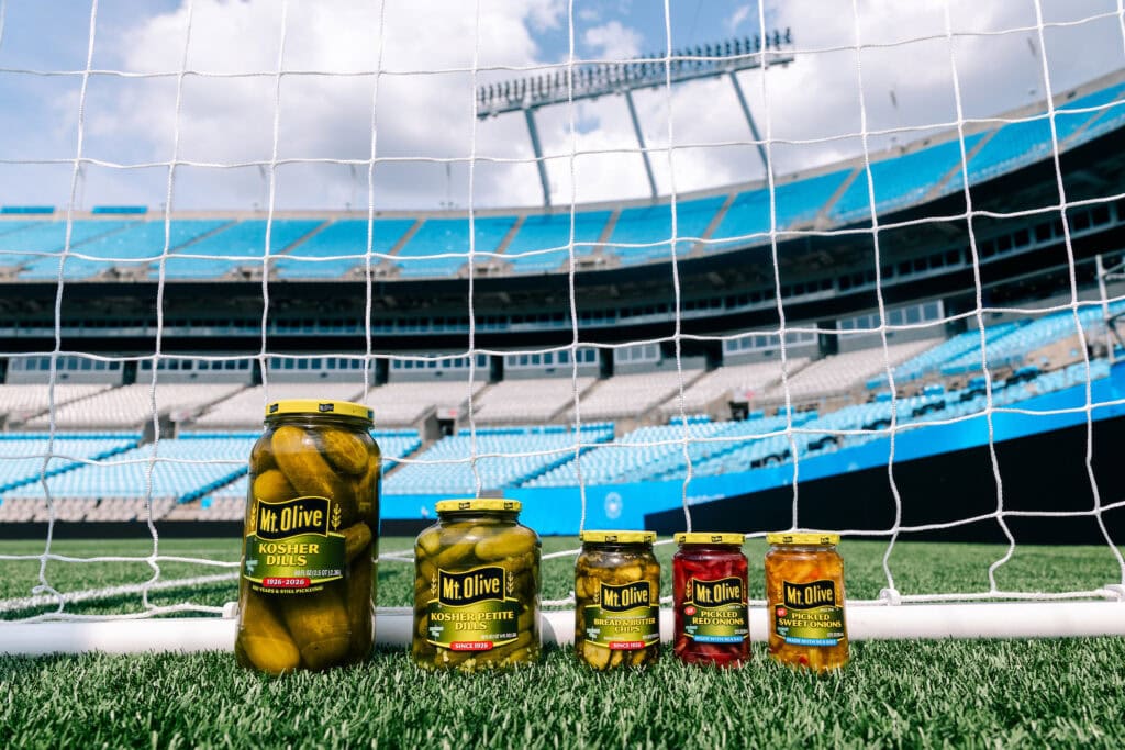 Mt Olive Pickles jars displayed on a soccer field with stadium in background.