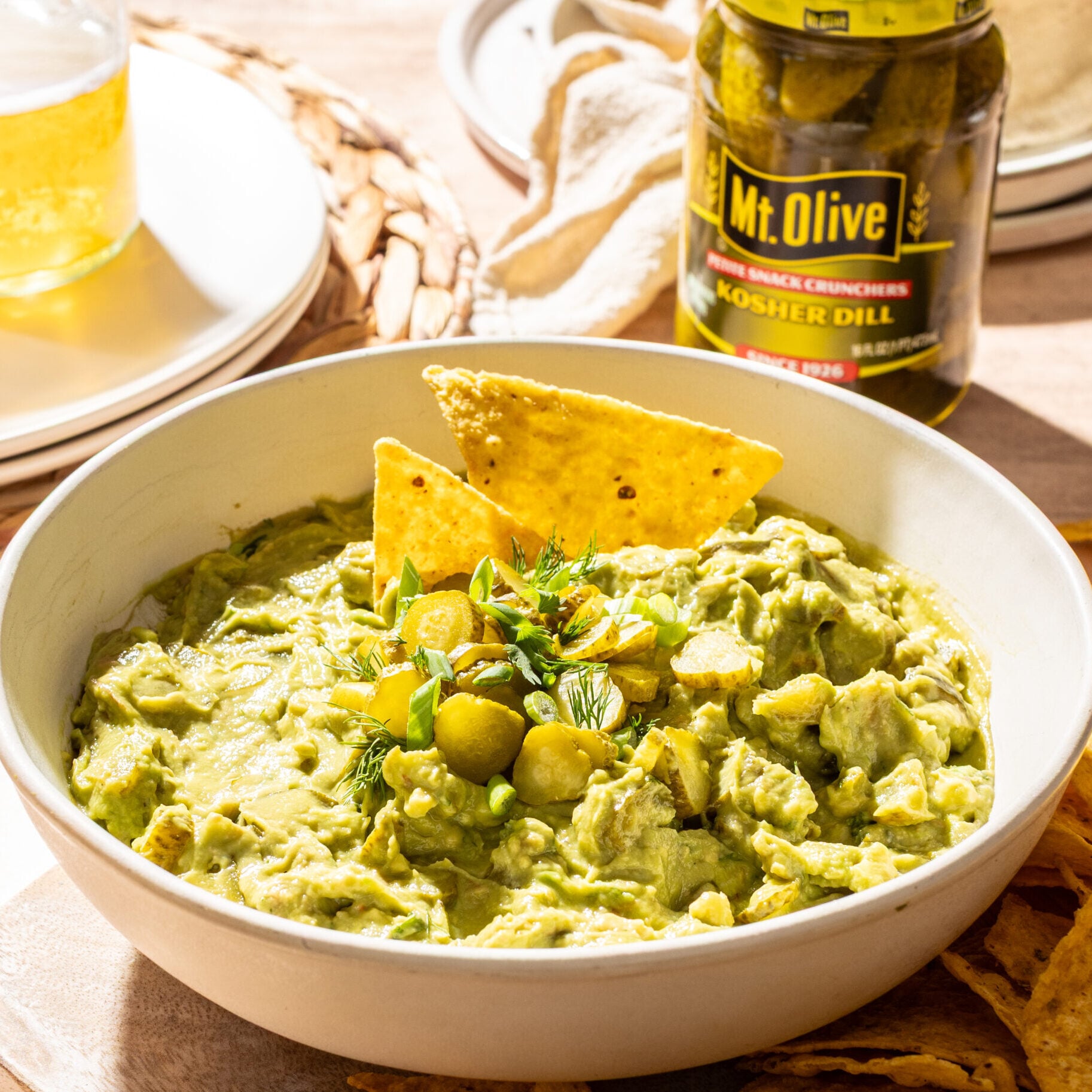 Creamy guacamole with pickles and tortilla chips on a wooden table.