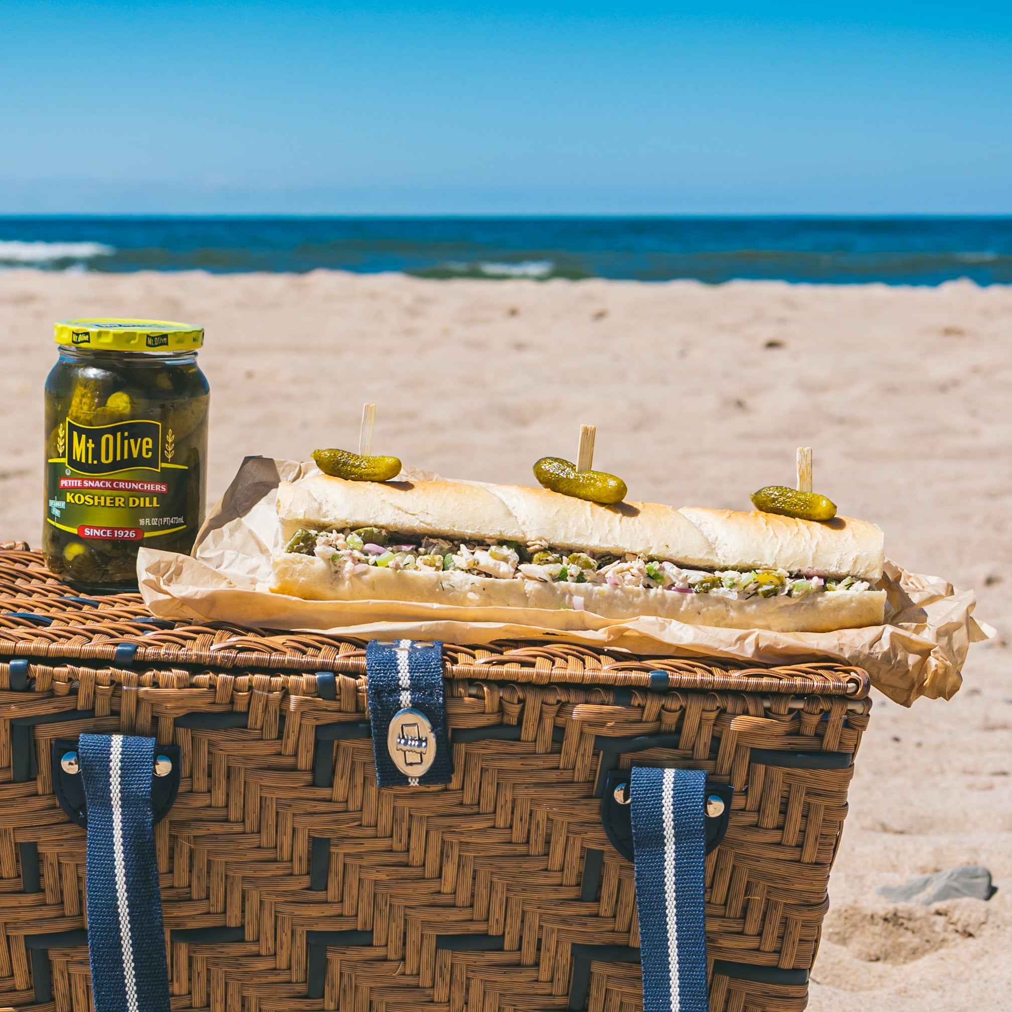 Submarine sandwich with pickles on a beach picnic basket.
