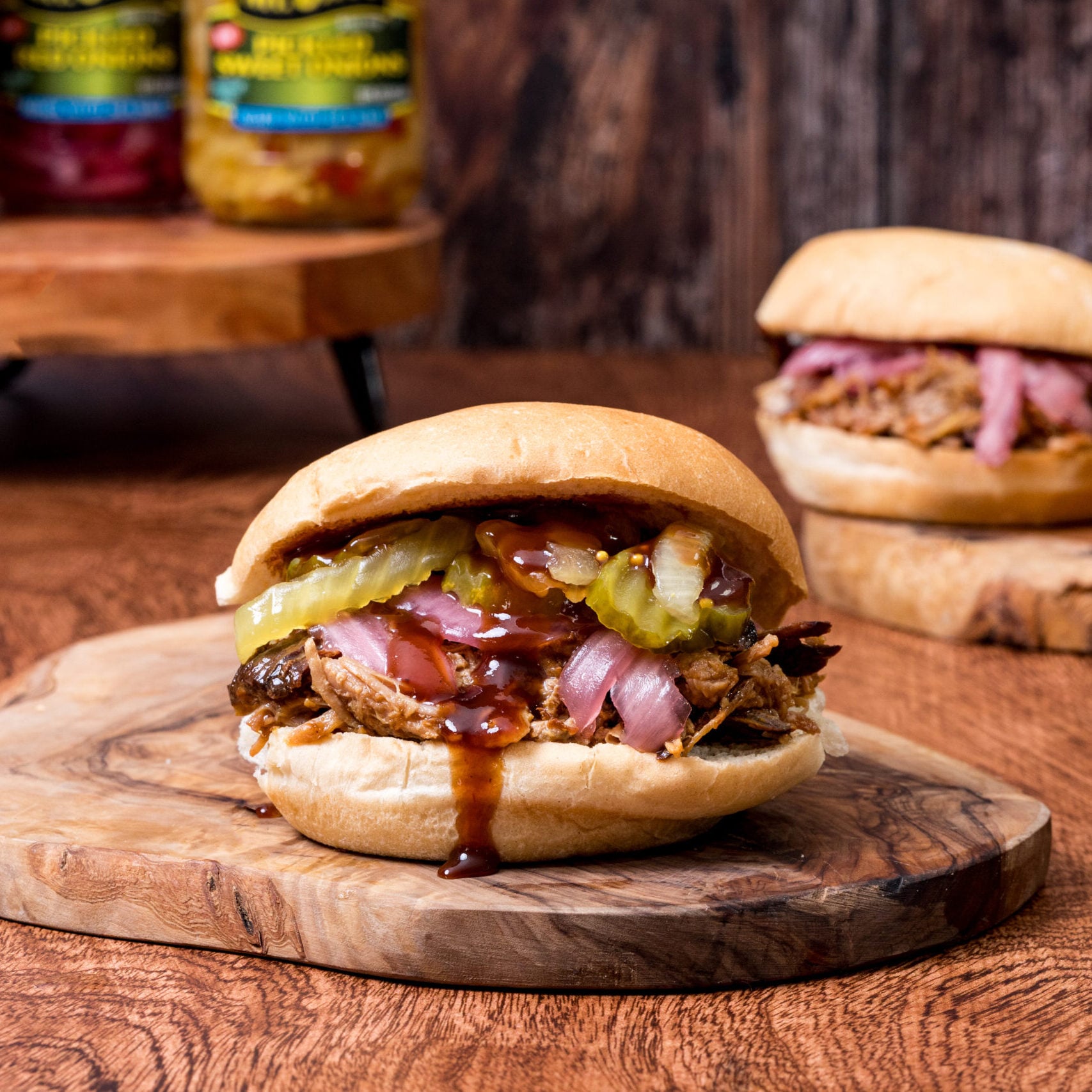Pulled pork sandwich with pickles and barbecue sauce on a wooden board.