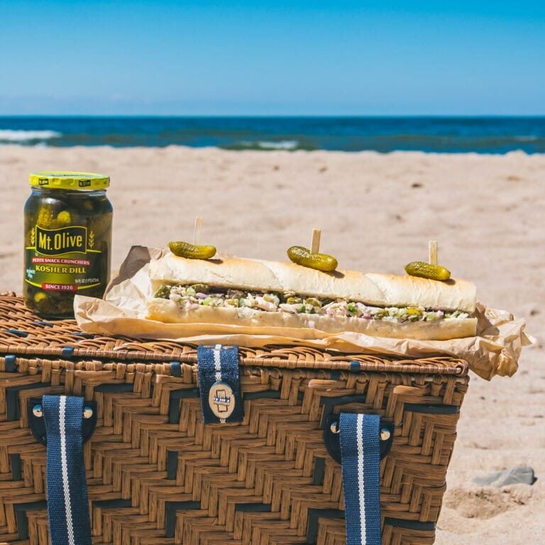Submarine sandwich with pickles on a beach picnic basket.