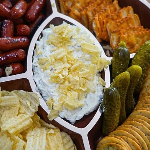 Ranch dill pickle dip with pickles, sausages, and crackers on a serving platter.
