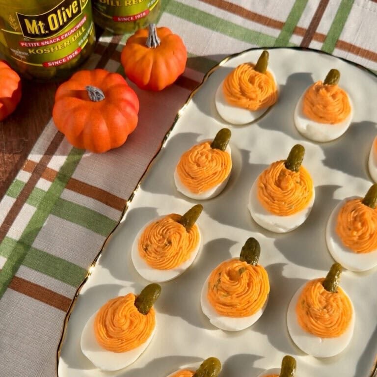 Mt Olive pickles beside deviled eggs with orange pumpkin swirls and pickle garnish.
